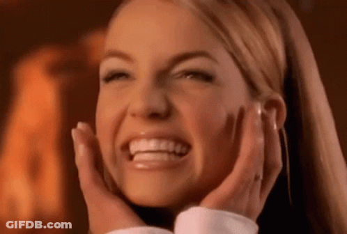A Woman Is Smiling And Holding Her Face With Her Hands . GIF