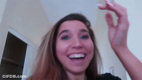 A Woman Is Smiling And Holding Her Hand Up In The Air While Looking At The Camera . GIF