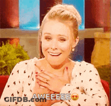 A Woman Is Smiling And Holding Her Hands To Her Chest While Wearing A Polka Dot Shirt . GIF