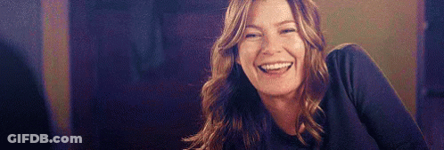 A Woman Is Smiling And Laughing While Sitting At A Table In A Dark Room . GIF