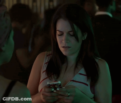 A Woman Is Smiling And Looking At Her Phone In A Dark Room GIF