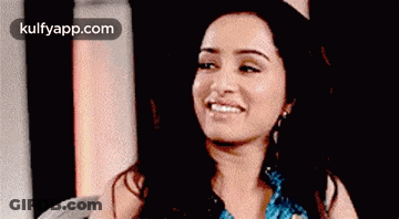 A Woman Is Smiling And Looking At The Camera While Sitting On A Chair . GIF