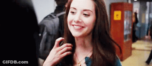 A Woman Is Smiling And Looking At The Camera While Standing In A Hallway . GIF
