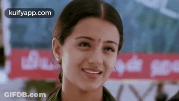 A Woman Is Smiling And Looking At The Camera While Standing In Front Of A Sign . GIF