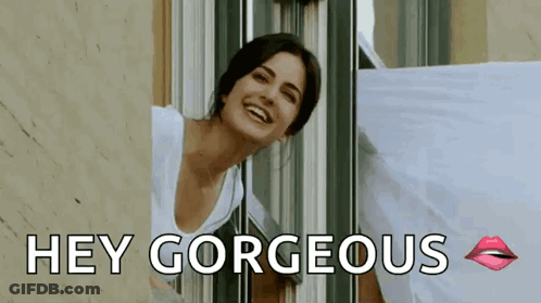 A Woman Is Smiling And Looking Out Of A Window With The Words `` Hey Gorgeous '' Written Below Her . GIF
