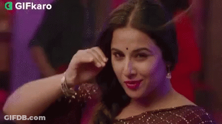 A Woman Is Smiling And Touching Her Hair In A Braid . GIF