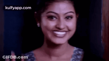 A Woman Is Smiling And Waving Her Hand In Front Of A Dark Background . GIF