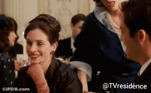 A Woman Is Smiling At A Man While Sitting At A Table In A Crowded Room . GIF