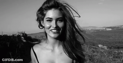 A Woman Is Smiling In A Black And White Photo While Her Hair Is Blowing In The Wind . GIF