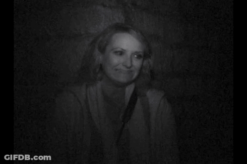 A Woman Is Smiling In A Black And White Photo While Sitting In A Dark Room . GIF