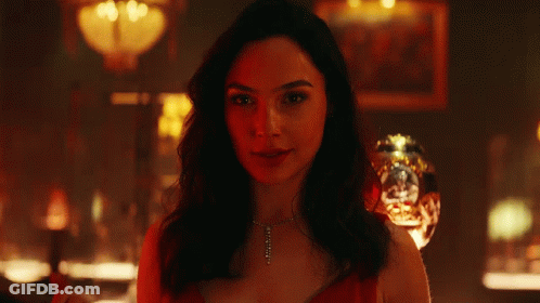 A Woman Is Smiling In A Dark Room With A Glass In The Background GIF