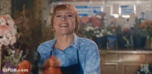 A Woman Is Smiling In A Flower Shop While Holding Flowers . GIF