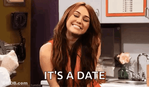 A Woman Is Smiling In A Kitchen With The Words `` It 'S A Date '' Written On Her Face . GIF