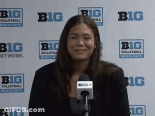 A Woman Is Smiling In Front Of A Big Volleyball Sign GIF