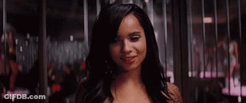 A Woman Is Smiling In Front Of A Crowd Of People In A Dark Room . GIF