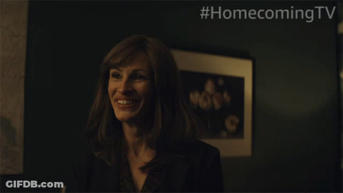 A Woman Is Smiling In Front Of A Framed Picture With #Homecomingtv Written On The Bottom GIF