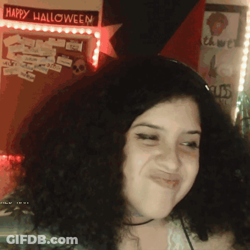 A Woman Is Smiling In Front Of A Happy Halloween Sign GIF