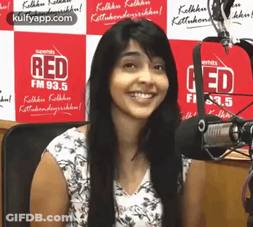 A Woman Is Smiling In Front Of A Microphone In Front Of A Red Fm Banner . GIF