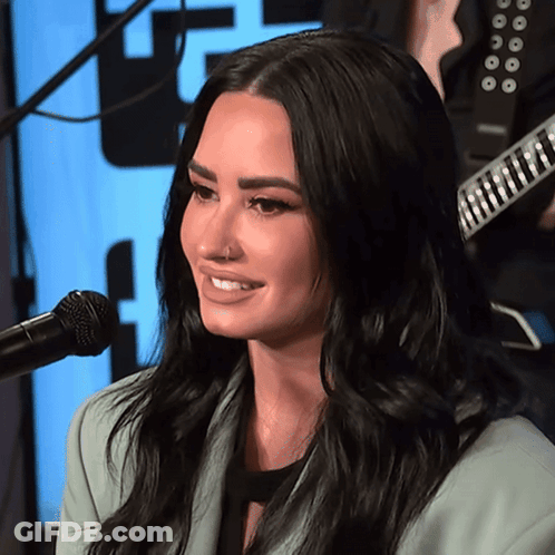 A Woman Is Smiling In Front Of A Microphone With A Guitar In The Background GIF