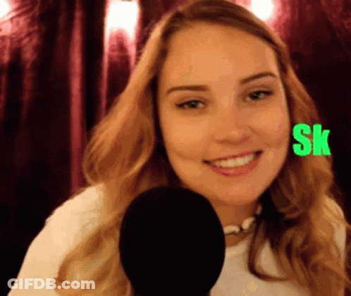A Woman Is Smiling In Front Of A Microphone With The Letters Sk On Her Face GIF
