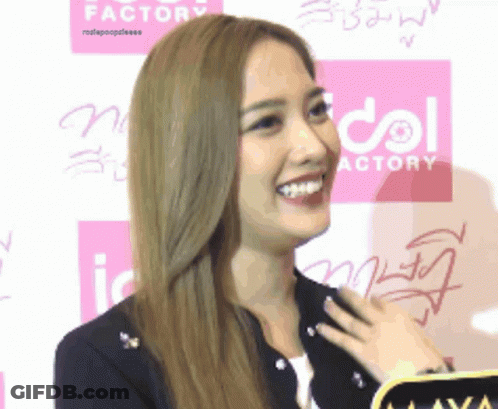 A Woman Is Smiling In Front Of A Pink Sign That Says Idol Actory GIF