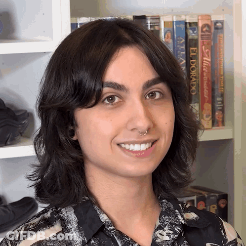 A Woman Is Smiling In Front Of A Shelf With Books Including El Dorado GIF