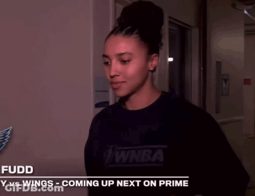 A Woman Is Smiling In Front Of A Sign That Says Fuddy Vs Wings Coming Up Next On Prime GIF