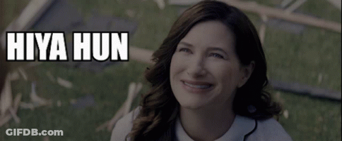A Woman Is Smiling In Front Of A Sign That Says " Hiya Hun " GIF
