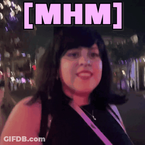 A Woman Is Smiling In Front Of A Sign That Says [ Mhm ] On It GIF