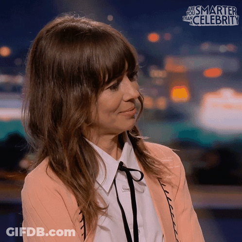 A Woman Is Smiling In Front Of A Sign That Says Smarter Than Celebrity GIF