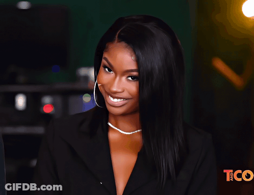 A Woman Is Smiling In Front Of A Tco Sign GIF