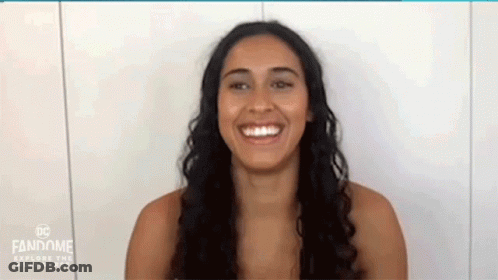 A Woman Is Smiling In Front Of A White Wall . GIF
