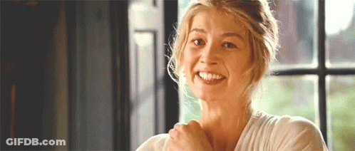 A Woman Is Smiling In Front Of A Window While Holding Her Arm Over Her Shoulder . GIF
