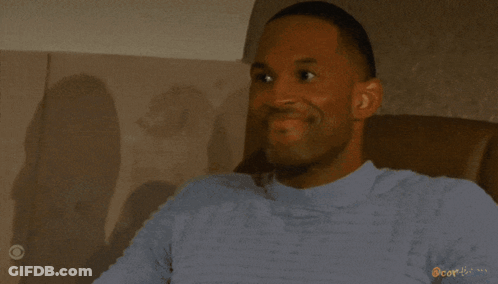 A Woman Is Smiling In Front Of A Window With Blinds And The Word Cor-Icon On The Bottom GIF
