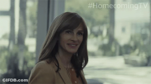 A Woman Is Smiling In Front Of A Window With #Homecomingtv Written On The Bottom GIF