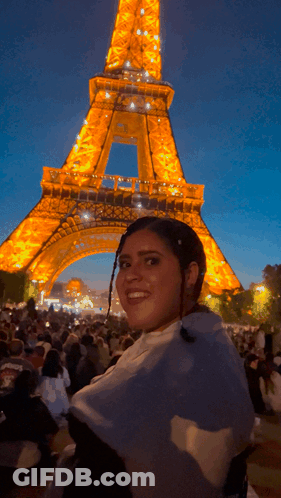 A Woman Is Smiling In Front Of The Eiffel Tower At Night GIF