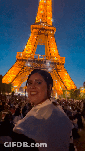 A Woman Is Smiling In Front Of The Eiffel Tower At Night GIF