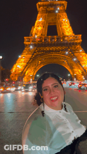 A Woman Is Smiling In Front Of The Eiffel Tower GIF
