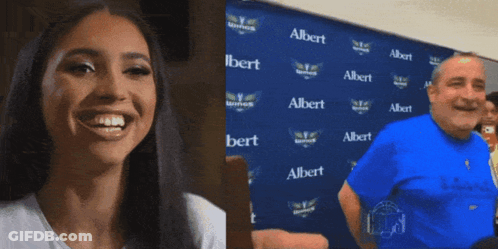 A Woman Is Smiling Next To A Man In Front Of A Wall With Albert Written On It GIF