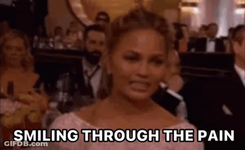 A Woman Is Smiling Through The Pain While Sitting In Front Of A Crowd . GIF