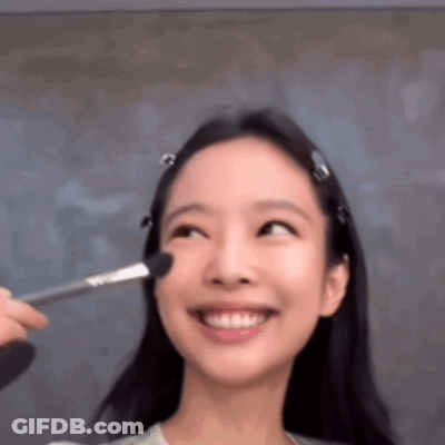 A Woman Is Smiling While Getting Her Makeup Done With A Brush On Her Face . GIF