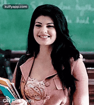A Woman Is Smiling While Holding A Book In Front Of A Blackboard . GIF