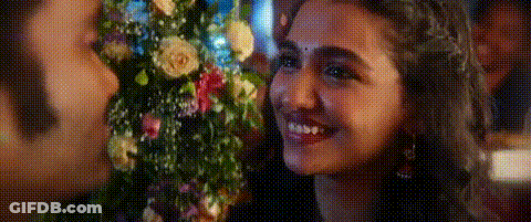 A Woman Is Smiling While Holding A Bouquet Of Flowers In Front Of A Man . GIF