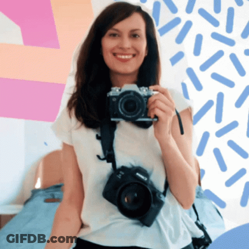 A Woman Is Smiling While Holding A Camera That Says Canon On It GIF