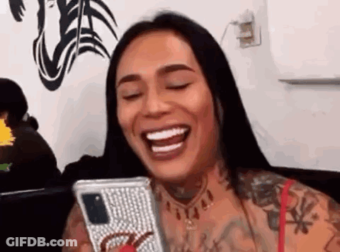 A Woman Is Smiling While Holding A Cell Phone In Her Hand . GIF