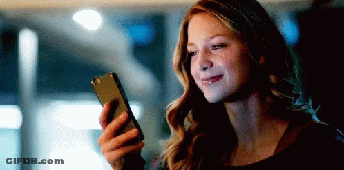 A Woman Is Smiling While Holding A Cell Phone In Her Hand . GIF