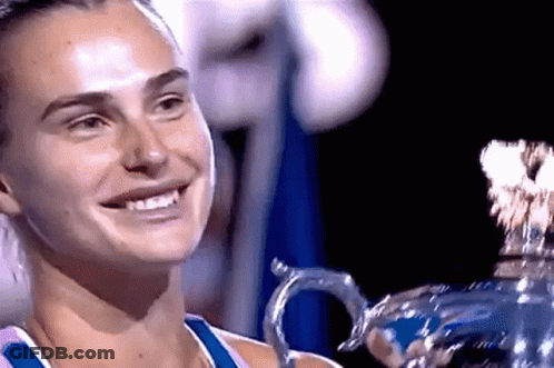 A Woman Is Smiling While Holding A Trophy In Her Hands . GIF