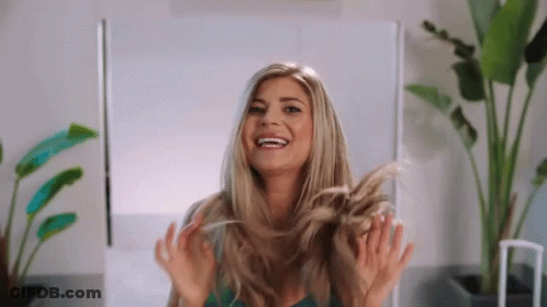 A Woman Is Smiling While Holding Her Hair In Her Hands GIF