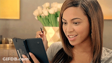 A Woman Is Smiling While Looking At A Tablet With A Pen In Her Hand GIF