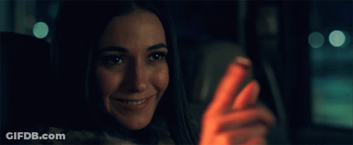 A Woman Is Smiling While Looking At Her Cell Phone GIF